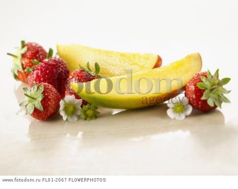 Mango, Mangifera indica. Two slices arranged with strawberries, Fragaria cultivar and flowers, on white marble. Selective focus.
