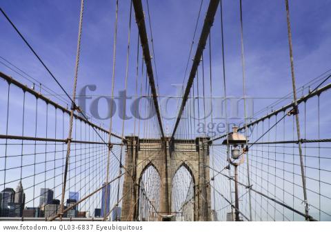 USA, New York, Brooklyn Bridge. View across bridge towards Manhattan skyline part framed by central stone tower and intersected by steel wires and suspension cables.