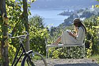 Woman reading book sitting on bench with sea view