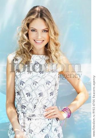 A young blonde woman wearing a grey-and-white patterned summer dress
