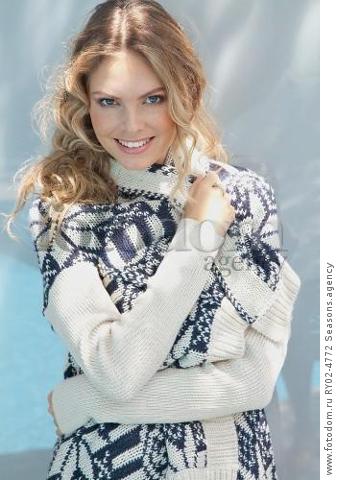 A young blonde woman wrapped in a blue-and-white knitted cardigan