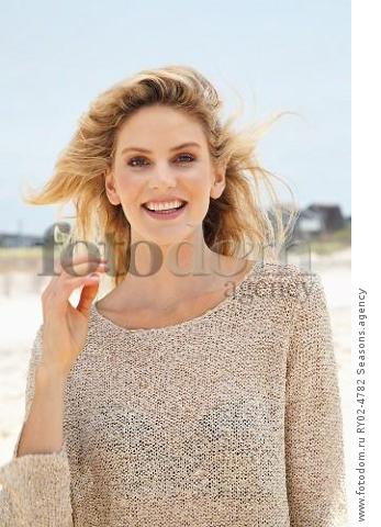 A young blonde woman on a beach wearing a beige knitted jumper