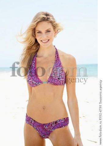 A young blonde woman on a beach wearing a purple bikini