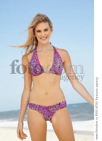 A young blonde woman on a beach wearing a purple bikini