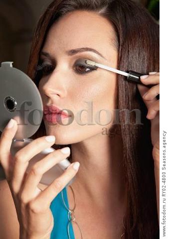 A brunette woman holding a compact mirror and applying eyeshadow