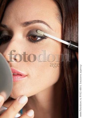 A brunette woman holding a compact mirror and applying eyeshadow