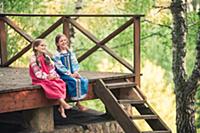 Девочки в русской народной одежде сидят на крыльце